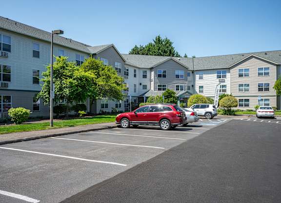 A red car is parked in a parking lot in front of apartment buildings.