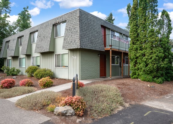 the front of a green apartment building with a sidewalk and landscaping