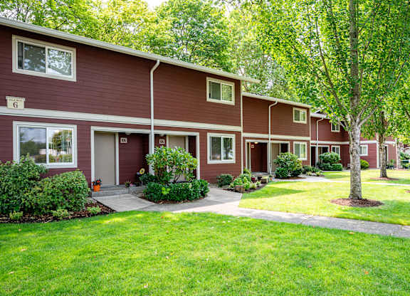 A red building with a white door and windows is surrounded by green trees.