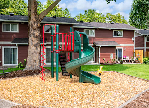 A red and green playground slide in front of a red house.