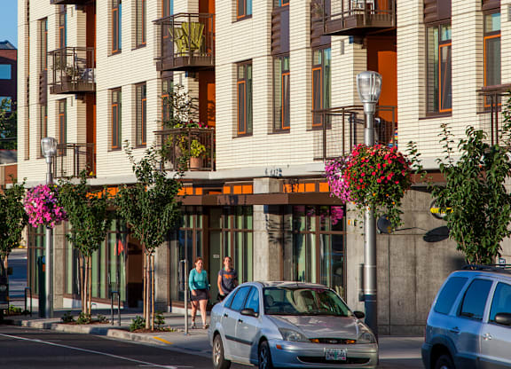 A car is parked on the street in front of a building with balconies.