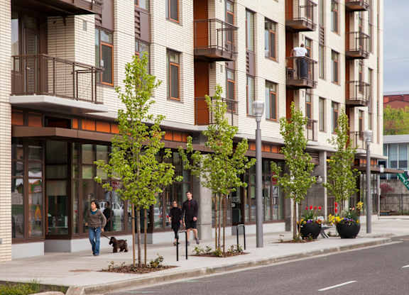A street view of a residential building with people walking on the sidewalk.