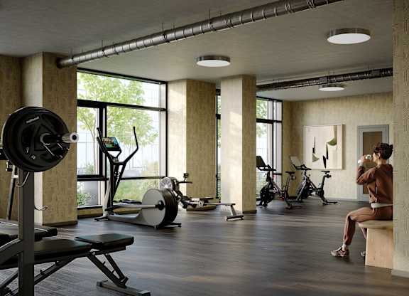 A person is sitting on a bench in a gym with a barbell on a squat rack.