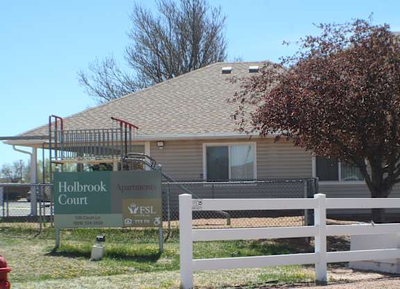 A sign for Holbrook Court apartments is in front of a building.
