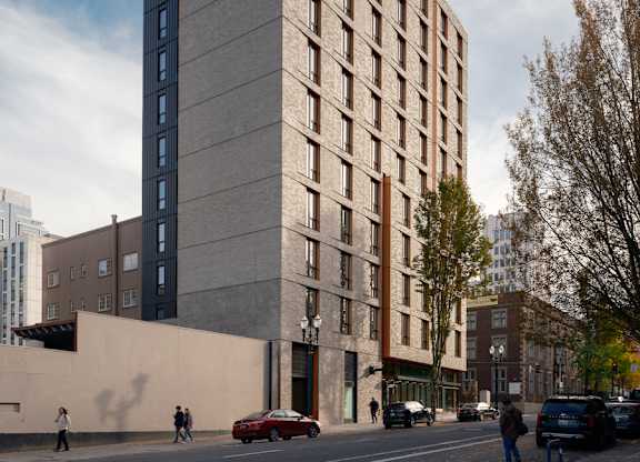 A tall building with a grey facade stands on a street corner with cars and pedestrians.