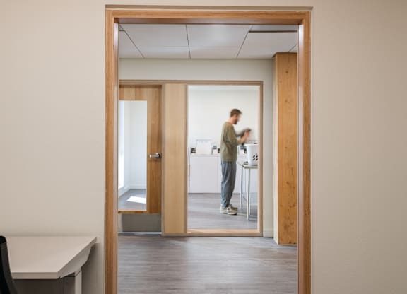 A man is standing in a room with a white desk and a mirror.