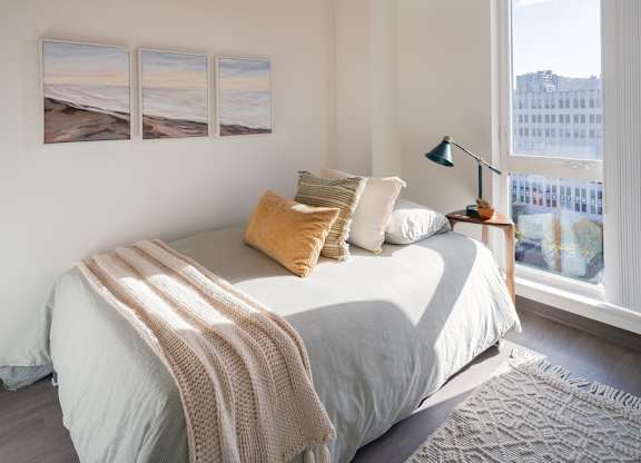 A bedroom with a bed, pillows, a blanket, a lamp, and pictures on the wall.