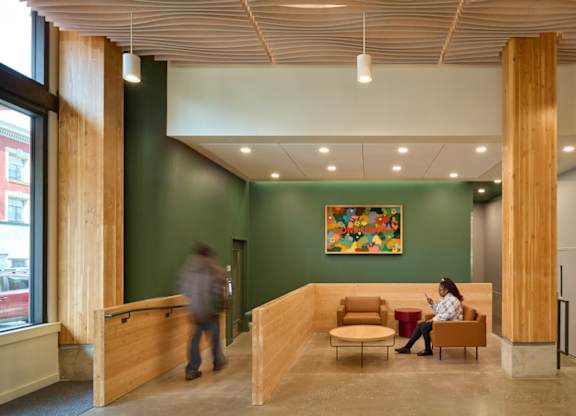A woman is sitting on a bench in a room with a green wall and a painting hanging on it.