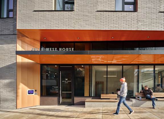 A man is walking past a building with a sign that reads "Jim West House.".