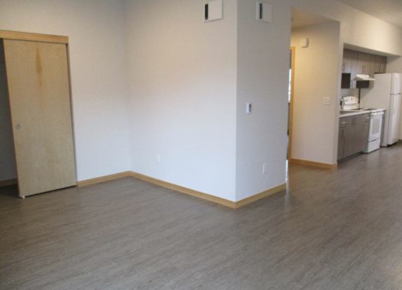 an empty living room with wood floors and a kitchen