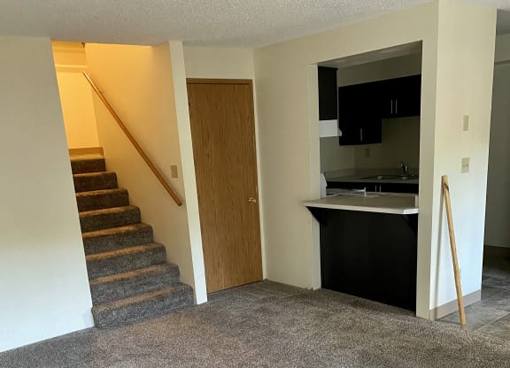 a carpeted living room with a staircase and a kitchen