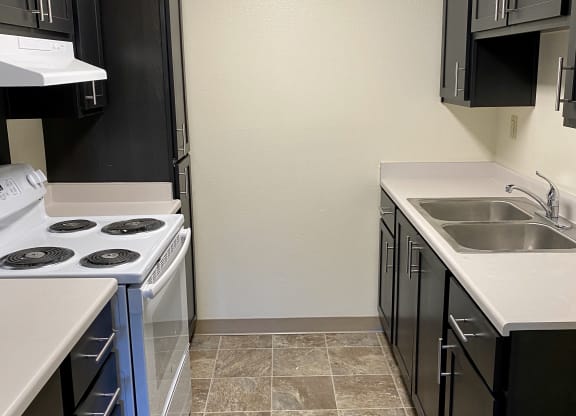 an empty kitchen with black cabinets and a white stove and sink