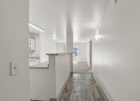 A long hallway with a white wall and a wooden floor.