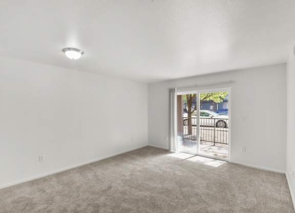A room with white walls and a carpeted floor with a doorway leading to a balcony.