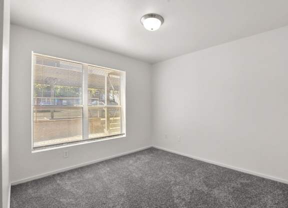 A room with a window and a grey carpet.