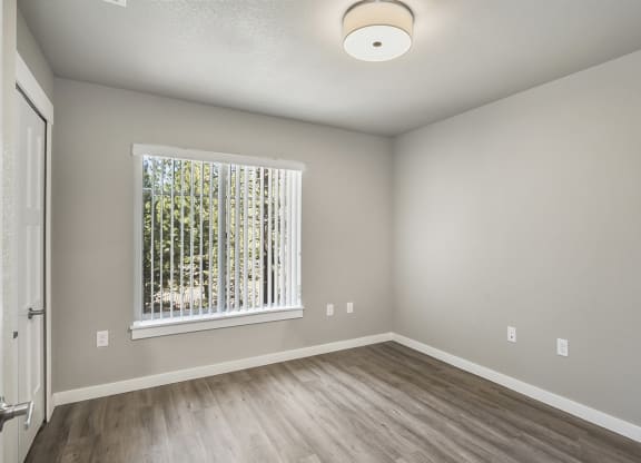 an empty bedroom with a large window and hardwood floors