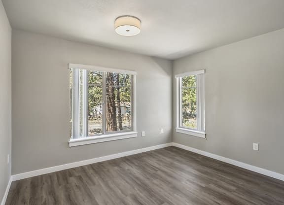 an empty bedroom with a large window and hardwood floors