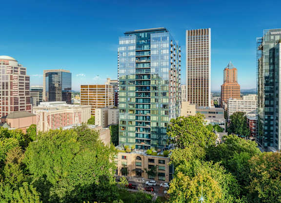 A cityscape with a mix of modern and older buildings, surrounded by lush green trees.