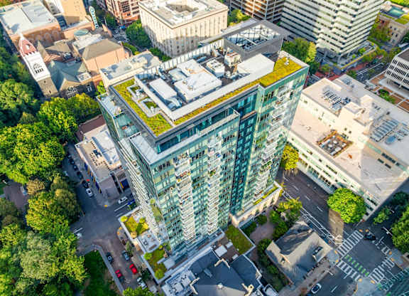 A modern building with a green roof is surrounded by other buildings and trees.