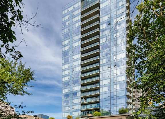 A modern glass building stands tall in a city park.