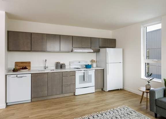 A modern kitchen with white appliances and a grey couch.