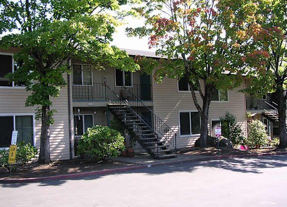 A tree with red leaves is in front of a beige building.