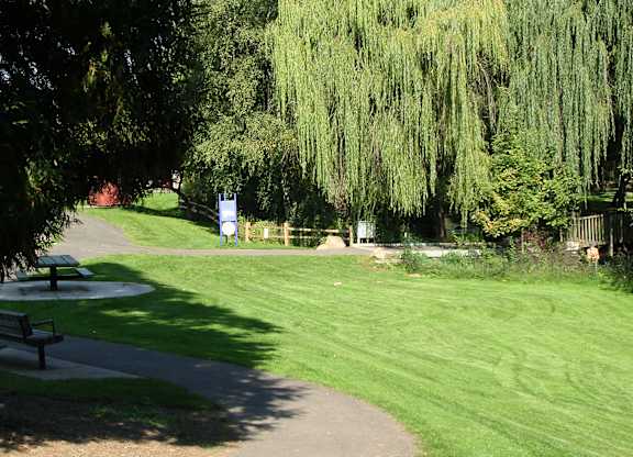 A park with a pathway, benches, and trees.
