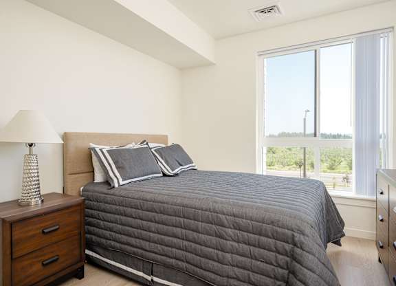 A bedroom with a large bed and a lamp on a nightstand.