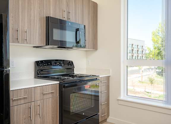 A black microwave is mounted on a wooden cabinet above a black stove.