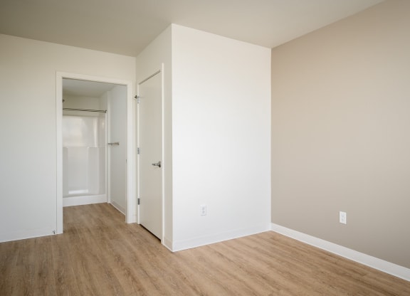 a bedroom with white walls and wood flooring and a closet