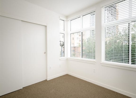 an empty bedroom with three windows and a closet