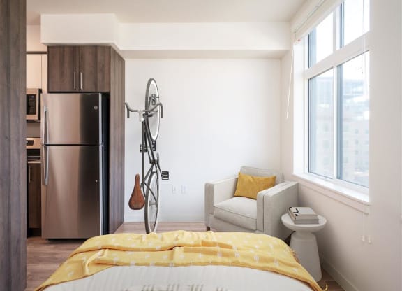 a bedroom with a bed and a refrigerator and a chair and a window