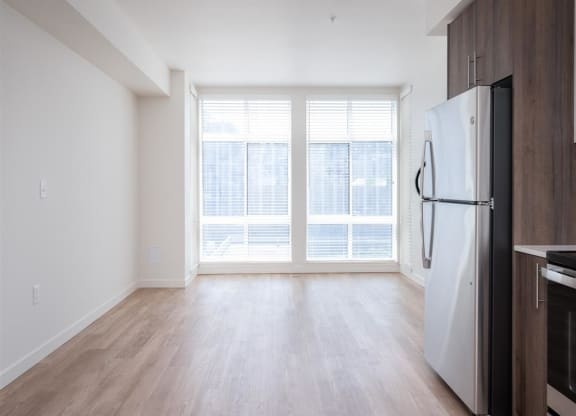 an empty living room with a large window and a refrigerator