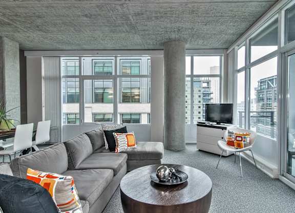 a living room with a gray couch and a tv in a room with large windows