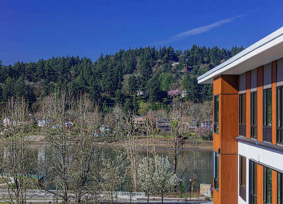 A building with a brown and white exterior sits in front of a body of water and a wooded area.
