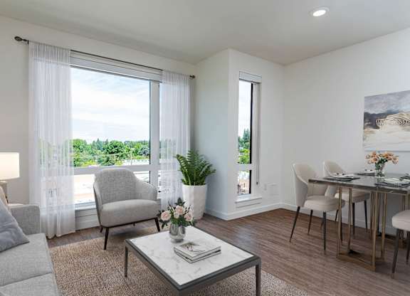 A living room with a grey couch, a coffee table, a chair, a dining table, and a painting on the wall.