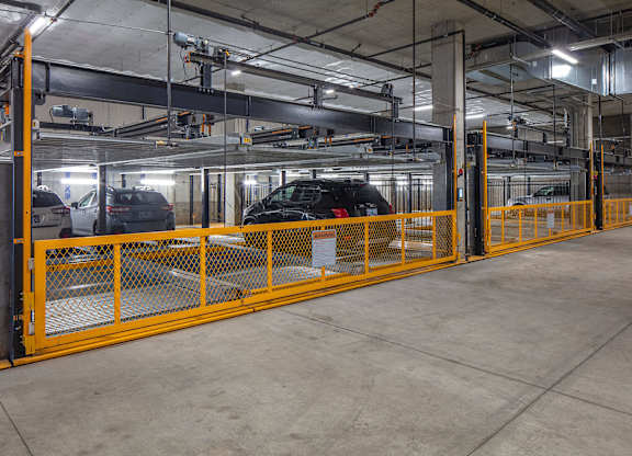 A parking garage with a yellow railing and a black car in the background.