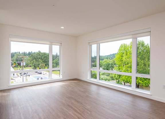 A large empty room with a view of a street and trees outside.