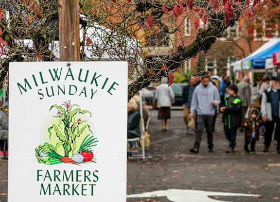 A sign for the Milwaukie Sunday Farmers Market is displayed on a pole.