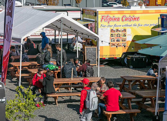 A food truck with the name Filipina Cuisine on it is parked at a food court.