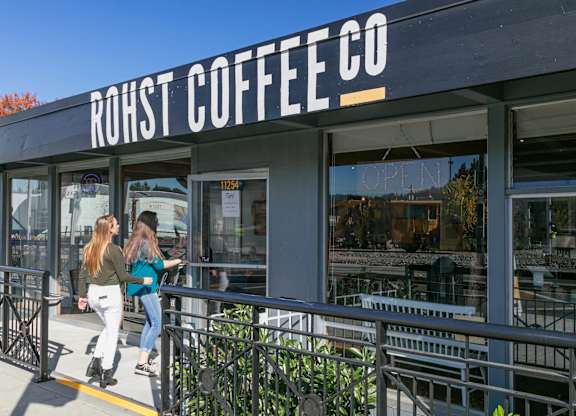 Two women are walking past a coffee shop named RoHst Coffee Co.