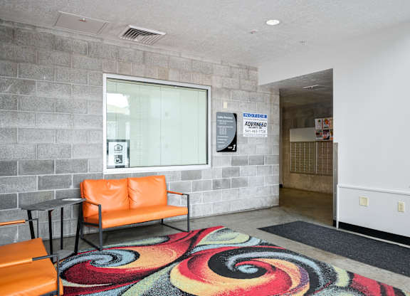 a lobby with orange chairs and a colorful rug and a window