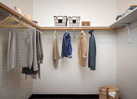 a closet with clothes hanging on the wall and a wooden shelf on the ceiling
