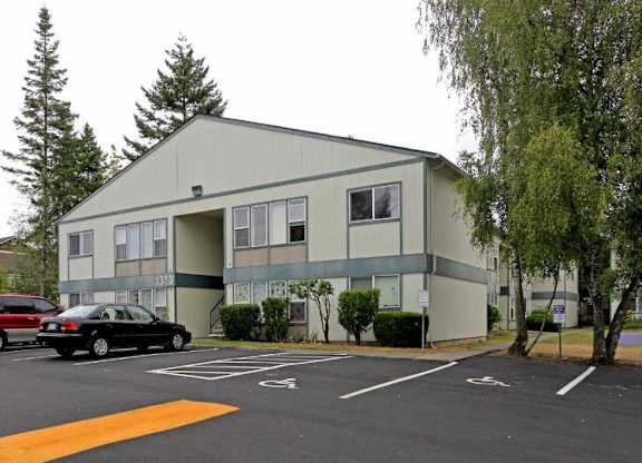 A parking lot in front of a grey building with a black car parked in the spot.