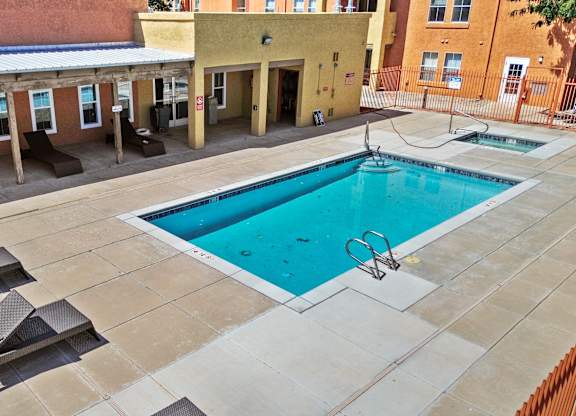 A swimming pool surrounded by sun loungers in a courtyard.