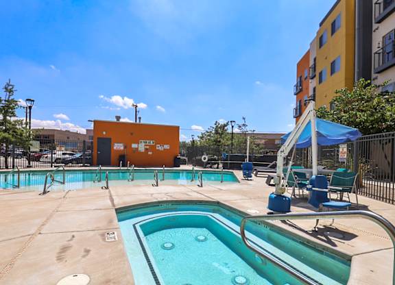 A small pool with a hot tub in front of a yellow building.
