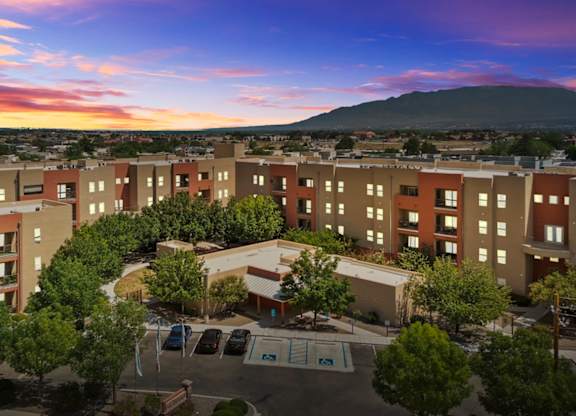 A sunset view of a large apartment complex with a parking lot in front.