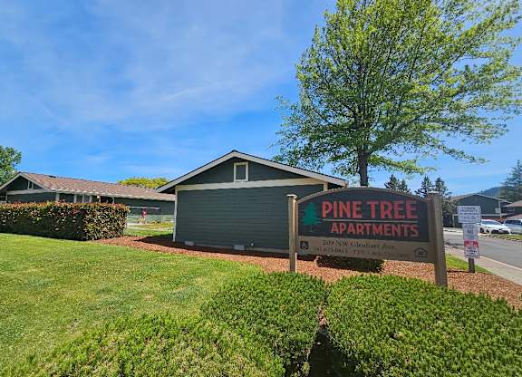 A sign for Pine Tree Apartments is in front of a green lawn.