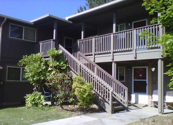 A brown house with a deck and stairs leading to the front door.