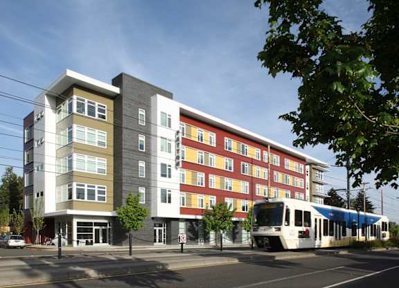 A modern multi-story building with a white and red facade stands next to a street with a tram.